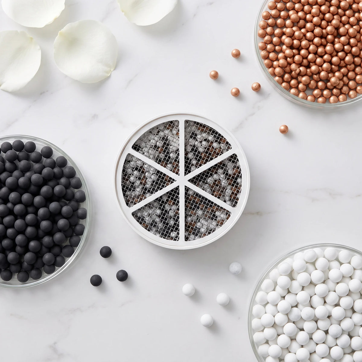 The Bath Ball disk cartridge with its six-segment stainless steel mesh face, beside glass dishes of black carbon, copper ERA and white ceramic spheres