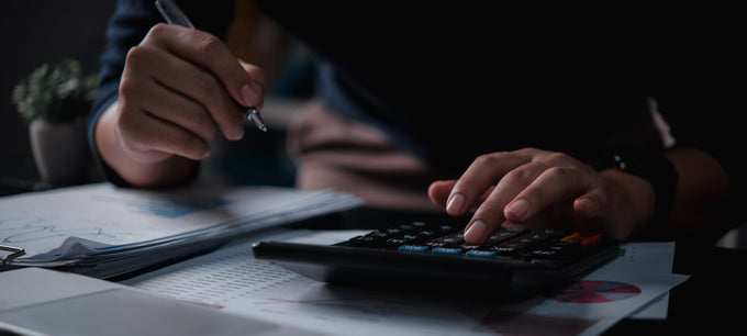 person with a pen in hand and using a calculator to budget