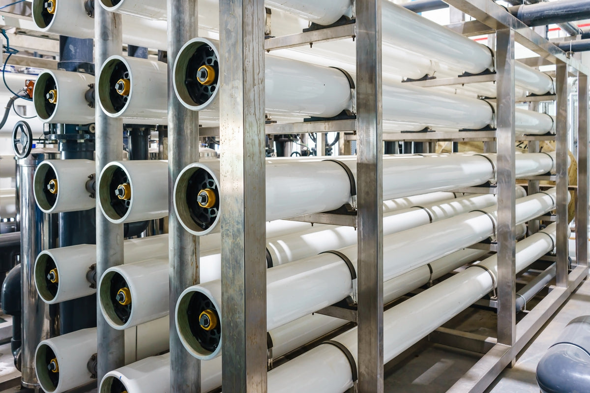 Rows of white reverse osmosis membrane pressure vessels with black end caps on stainless steel racks in a treatment plant