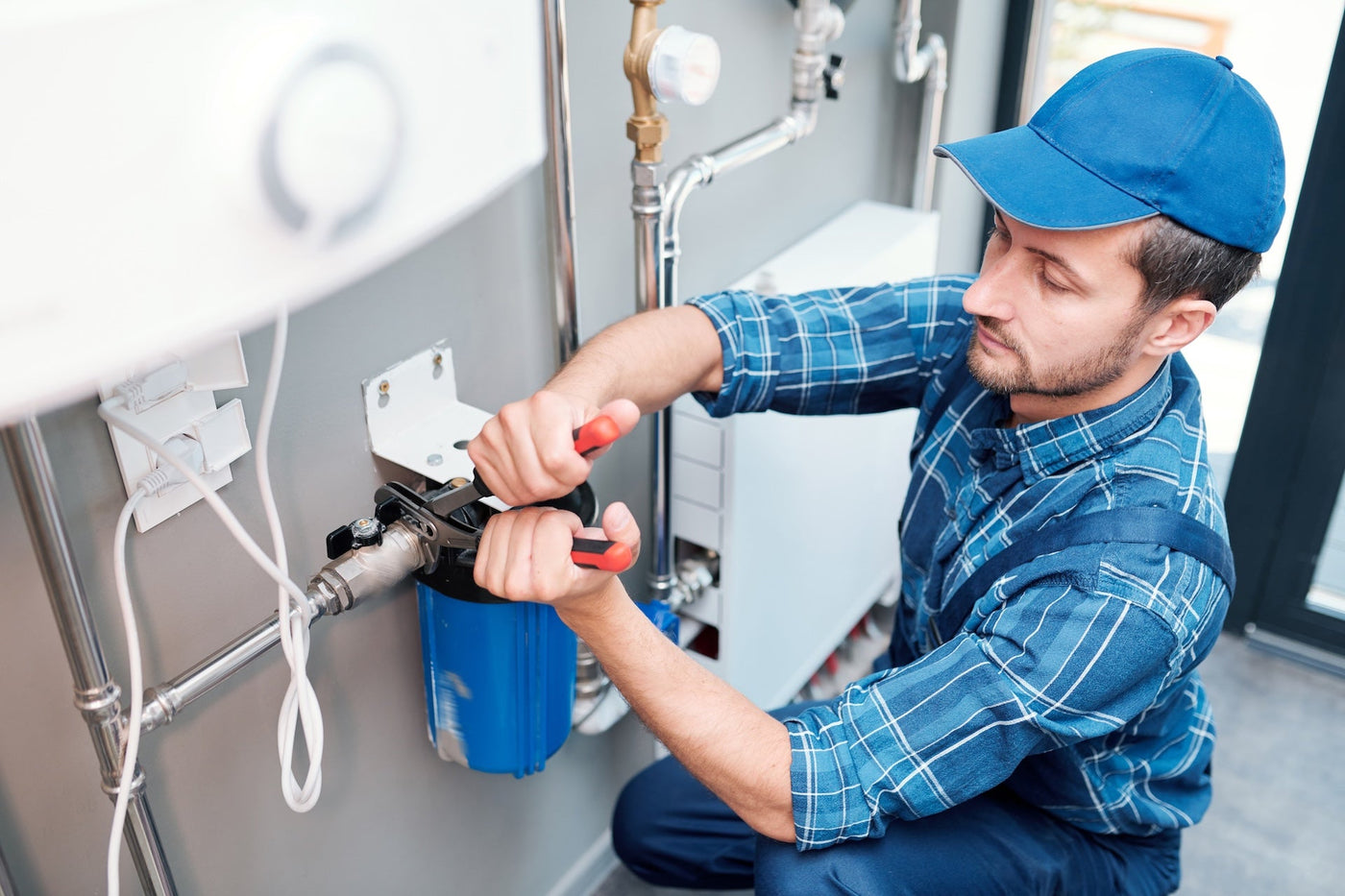 Technician installing a whole-house water filter housing on residential plumbing near a water heater