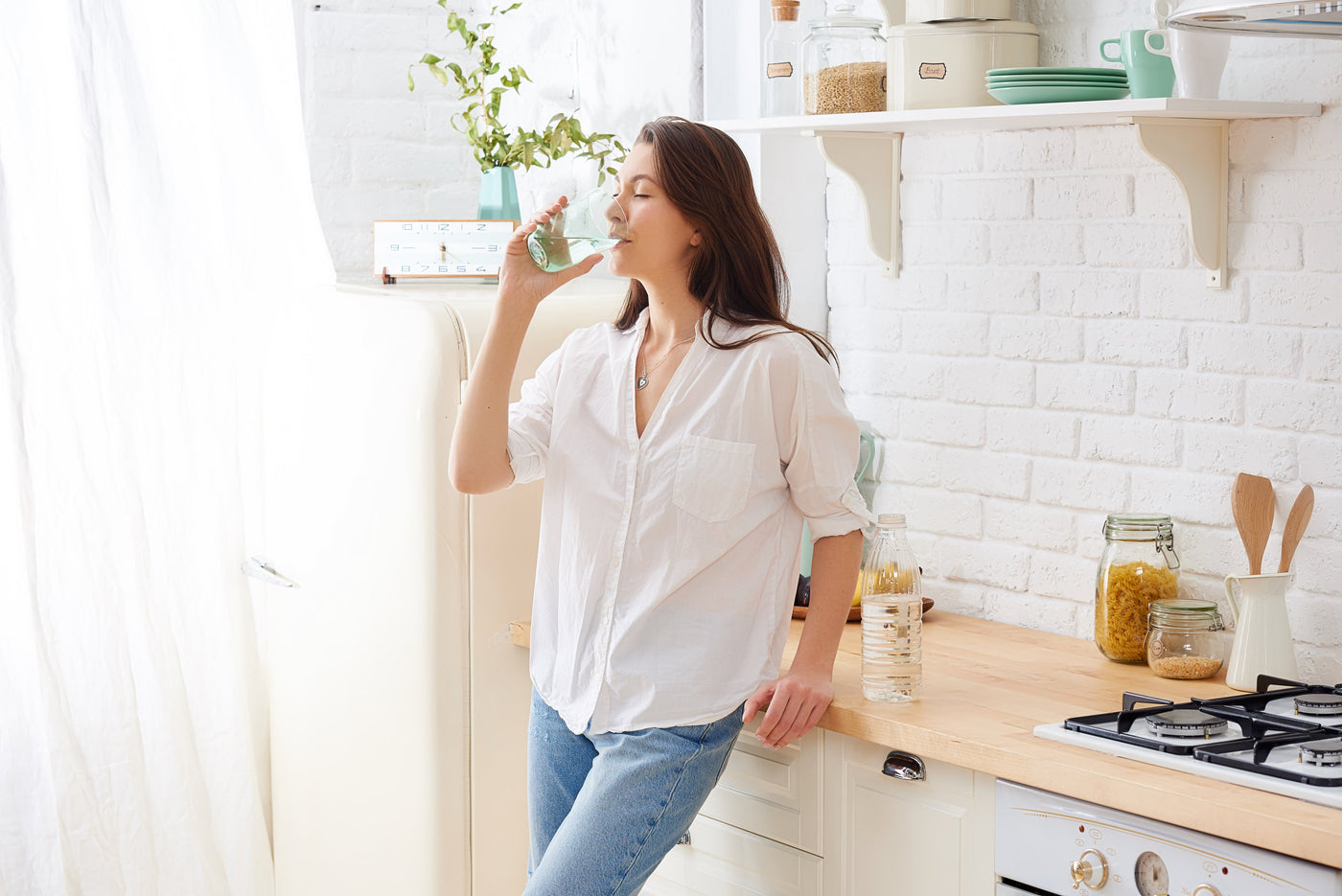 Woman drinking a glass of water in a bright kitchen while considering her state's water standards
