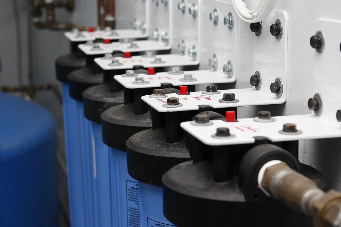 Row of Crystal Quest blue whole-house water filter housings on labeled mounting brackets in a utility room