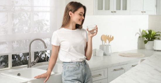 Woman drinking a glass of clean, clear water in a bright modern kitchen