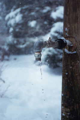 Frozen outdoor water tap dripping over snow in winter, a reminder to protect pipes and water systems from freezing