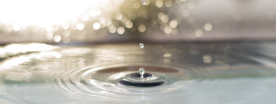 A single water droplet landing in a still pool and sending out concentric ripples, illustrating the weight and density of water
