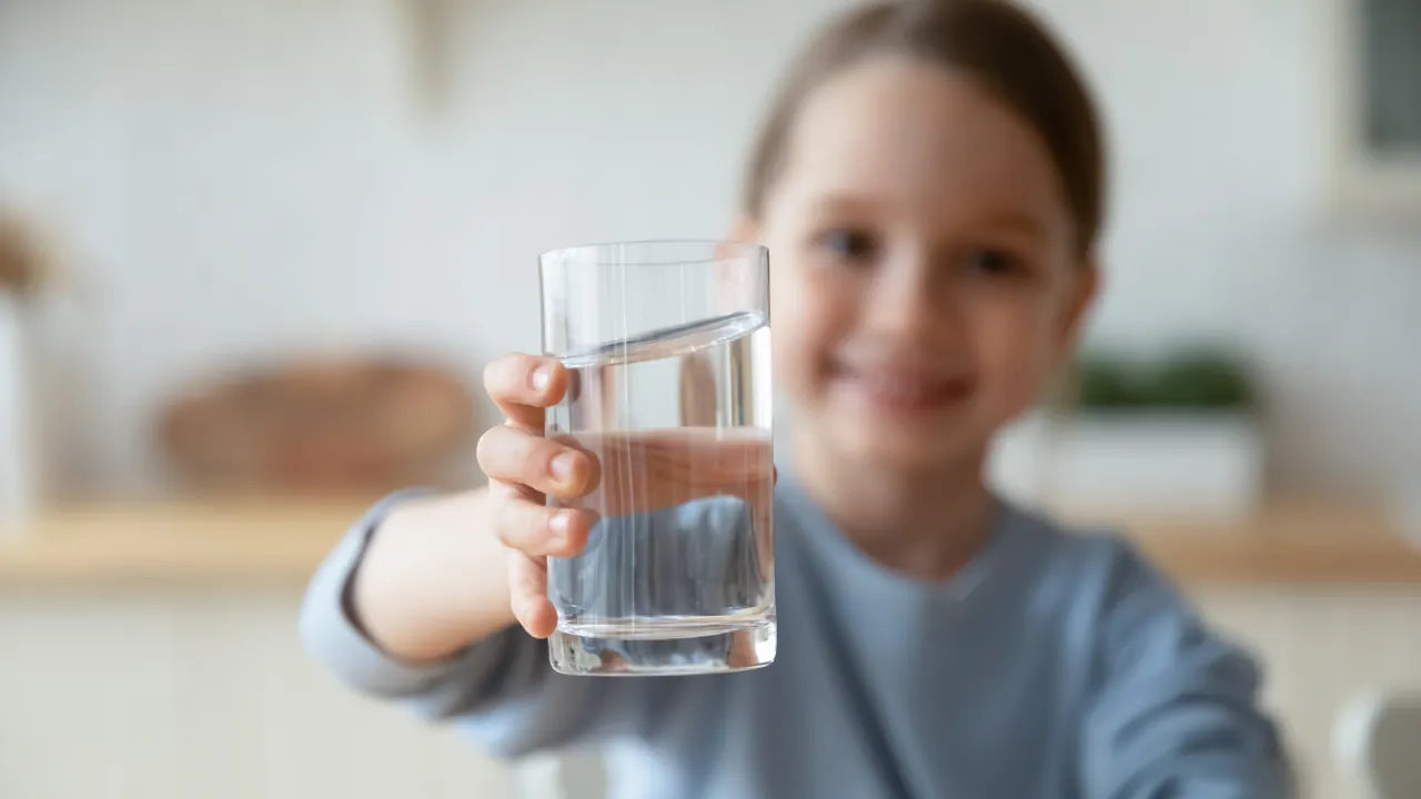 Smiling child in a bright kitchen holding out a clear glass of water