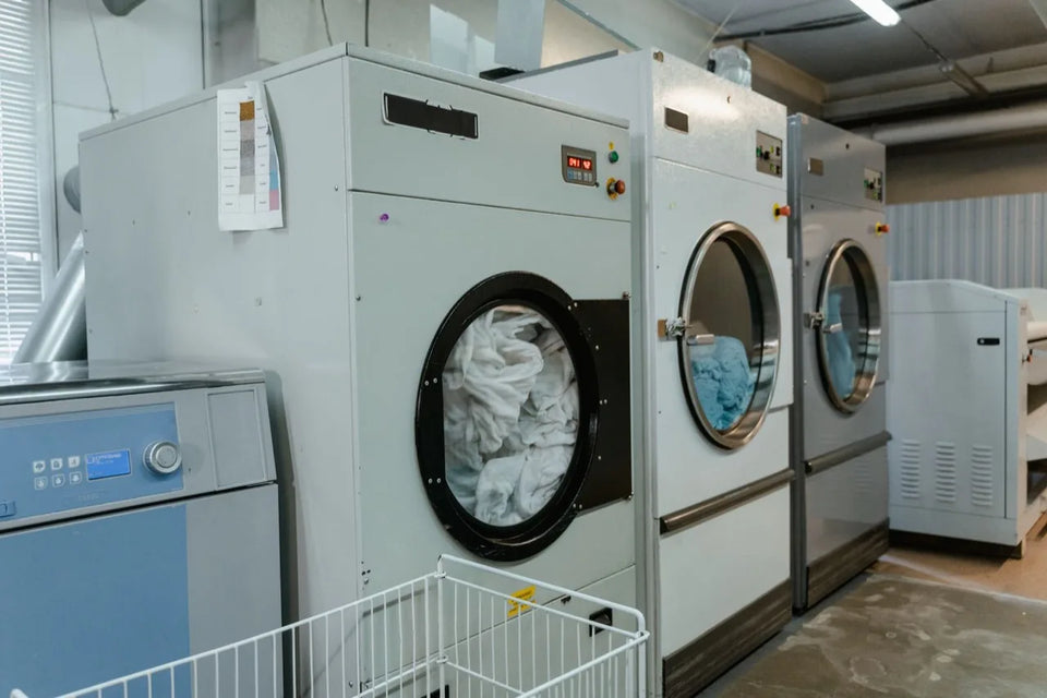 Industrial washer extractors loaded with white and blue linen in an on premise commercial laundry, with a flatwork ironer at right