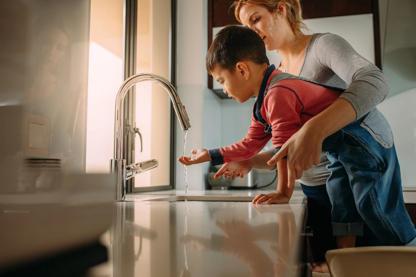 Mother and child using tap water at the kitchen sink, the water that EPA PFAS regulations are meant to protect