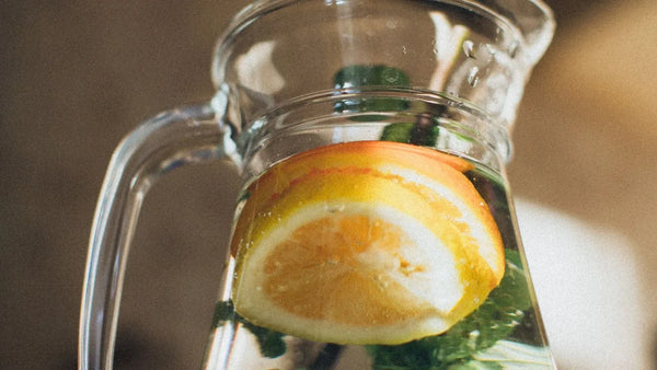 Glass pitcher of lemon water with a fresh lemon slice and mint