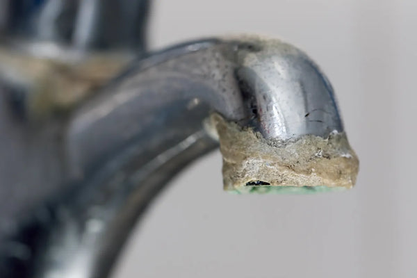 Chrome bathroom faucet spout heavily encrusted with hard water limescale and mineral buildup
