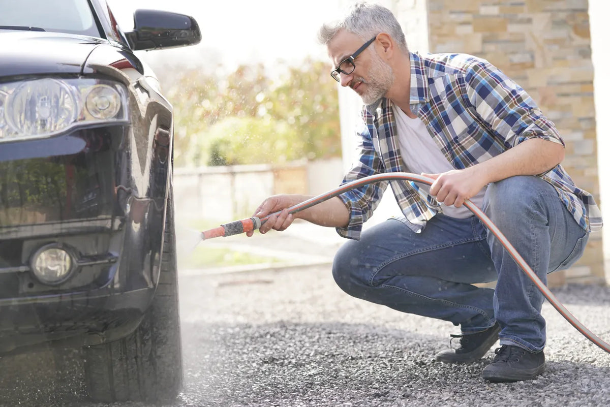 Person rinsing a dark car with a garden hose in a driveway
