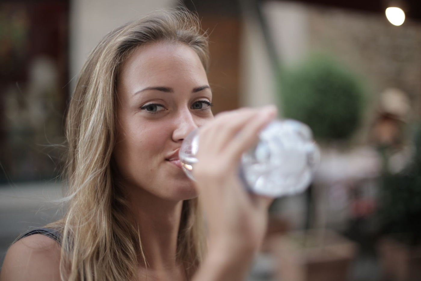A woman drinking bottled water from a clear plastic bottle, raising the question of whether bottled water contains PFAS