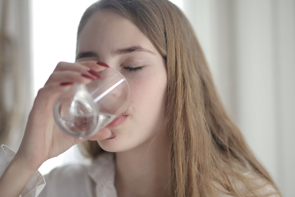 Young woman with her eyes closed sipping a glass of water in a bright room