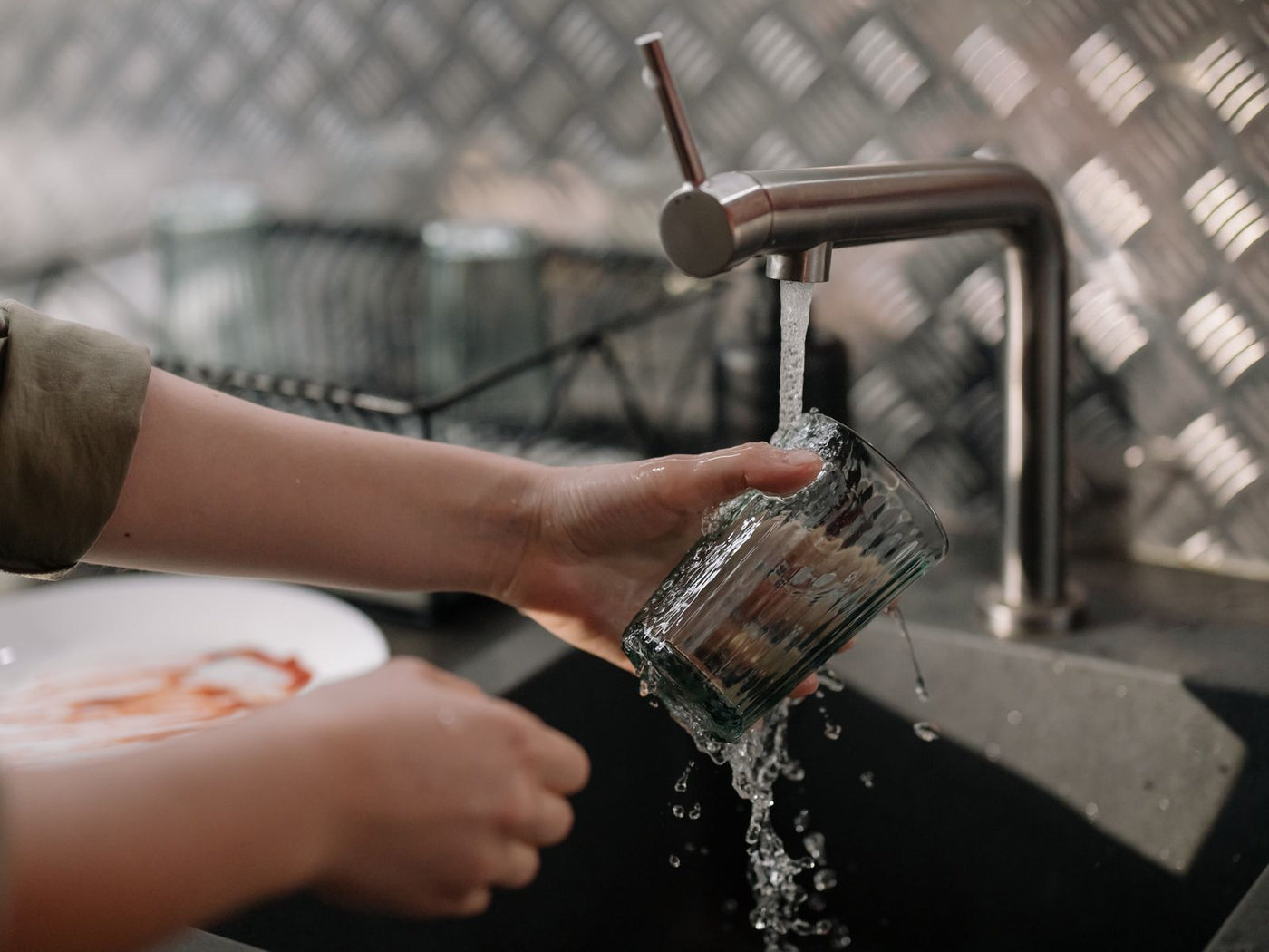 A hand filling a clear drinking glass with water from a kitchen faucet