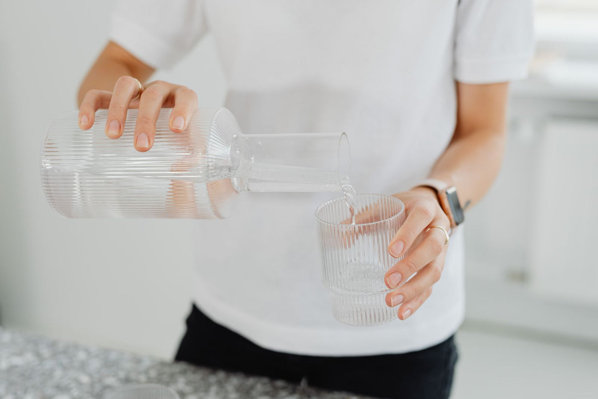 Parent carefully pouring clean filtered water from a carafe into a glass in a bright kitchen