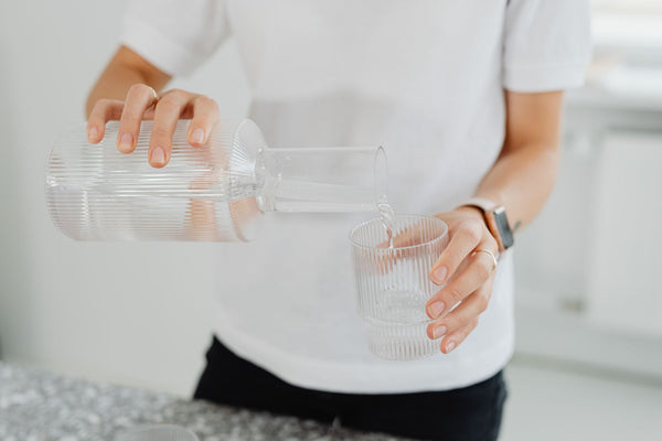 Parent carefully pouring clean filtered water from a carafe into a glass in a bright kitchen