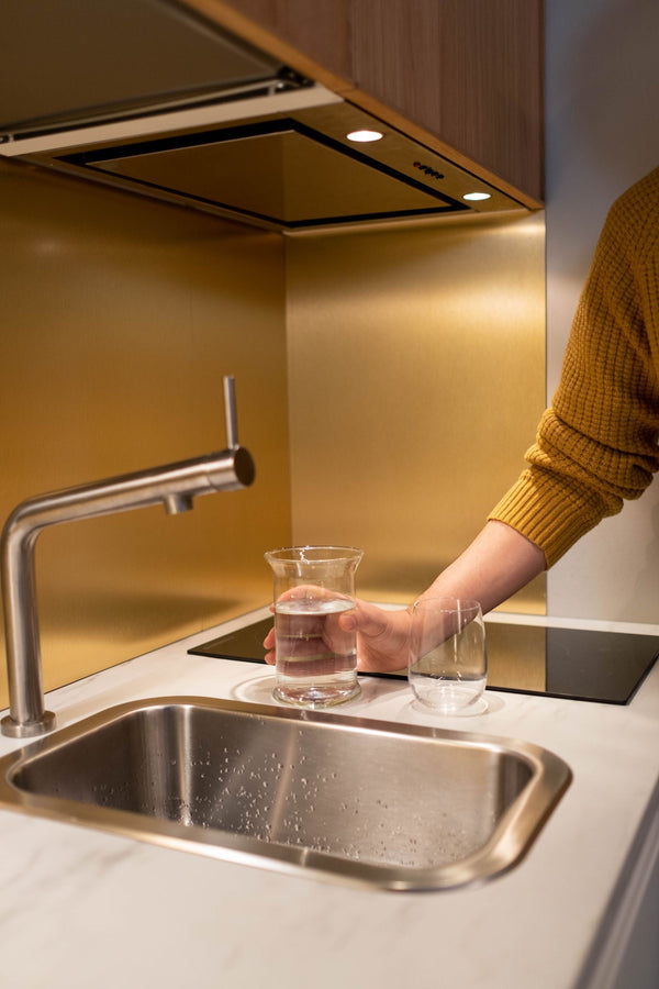 Glass of softened water set on the counter beside a modern kitchen faucet