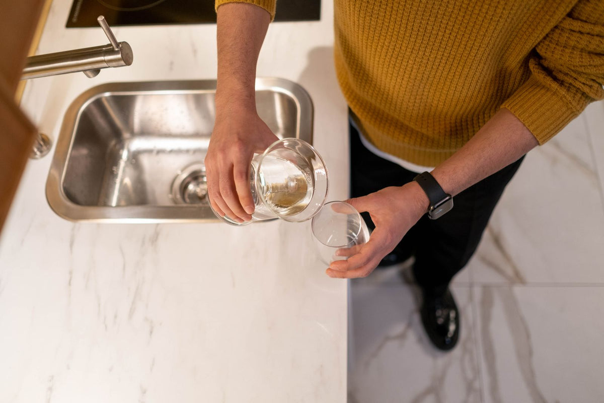 Overhead view of a person pouring a fresh glass of water at a modern kitchen sink