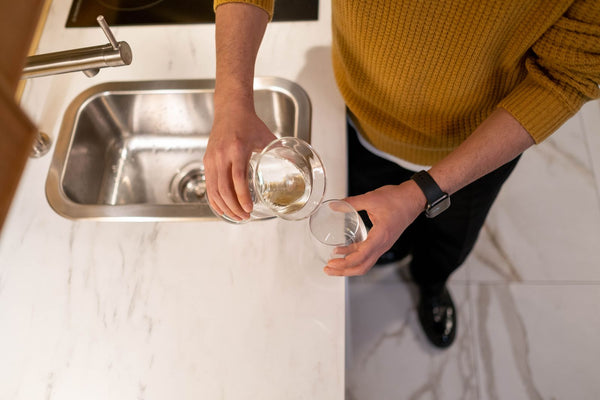 Overhead view of a person pouring a fresh glass of water at a modern kitchen sink