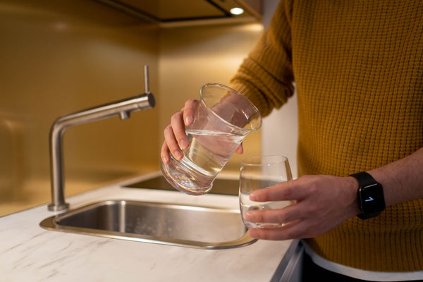 Person holding a freshly filled glass of clear water at a kitchen sink faucet