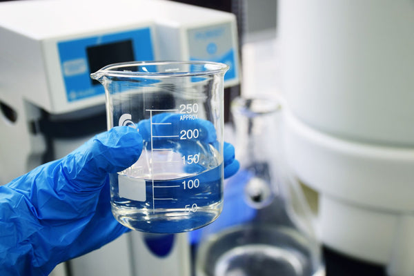Gloved laboratory technician holding a beaker of purified water beside analytical instruments