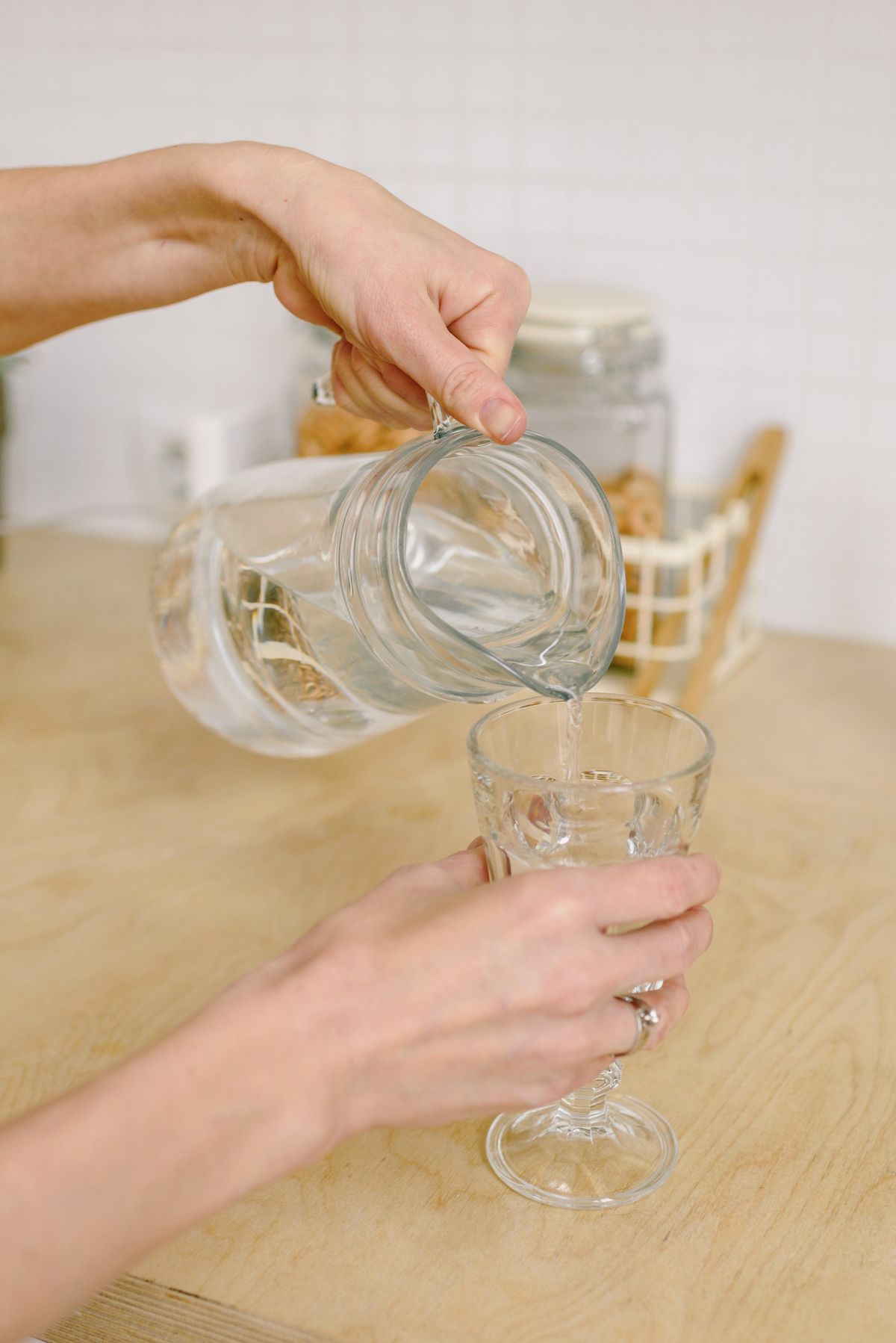 Clear water poured from a glass pitcher into a stemmed drinking glass on a kitchen counter