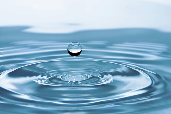 Single water droplet falling into clear blue water with concentric ripples, illustrating purified water and dissolved minerals