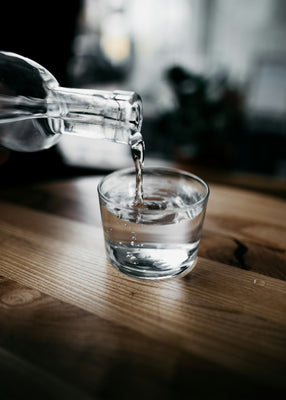 Clean filtered water being poured into a glass on a wooden kitchen table