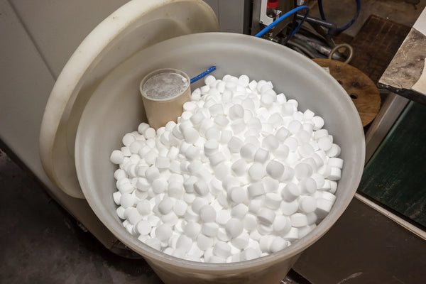 Open water softener brine tank filled with white salt pellets, brine well tube at the side, in a utility space