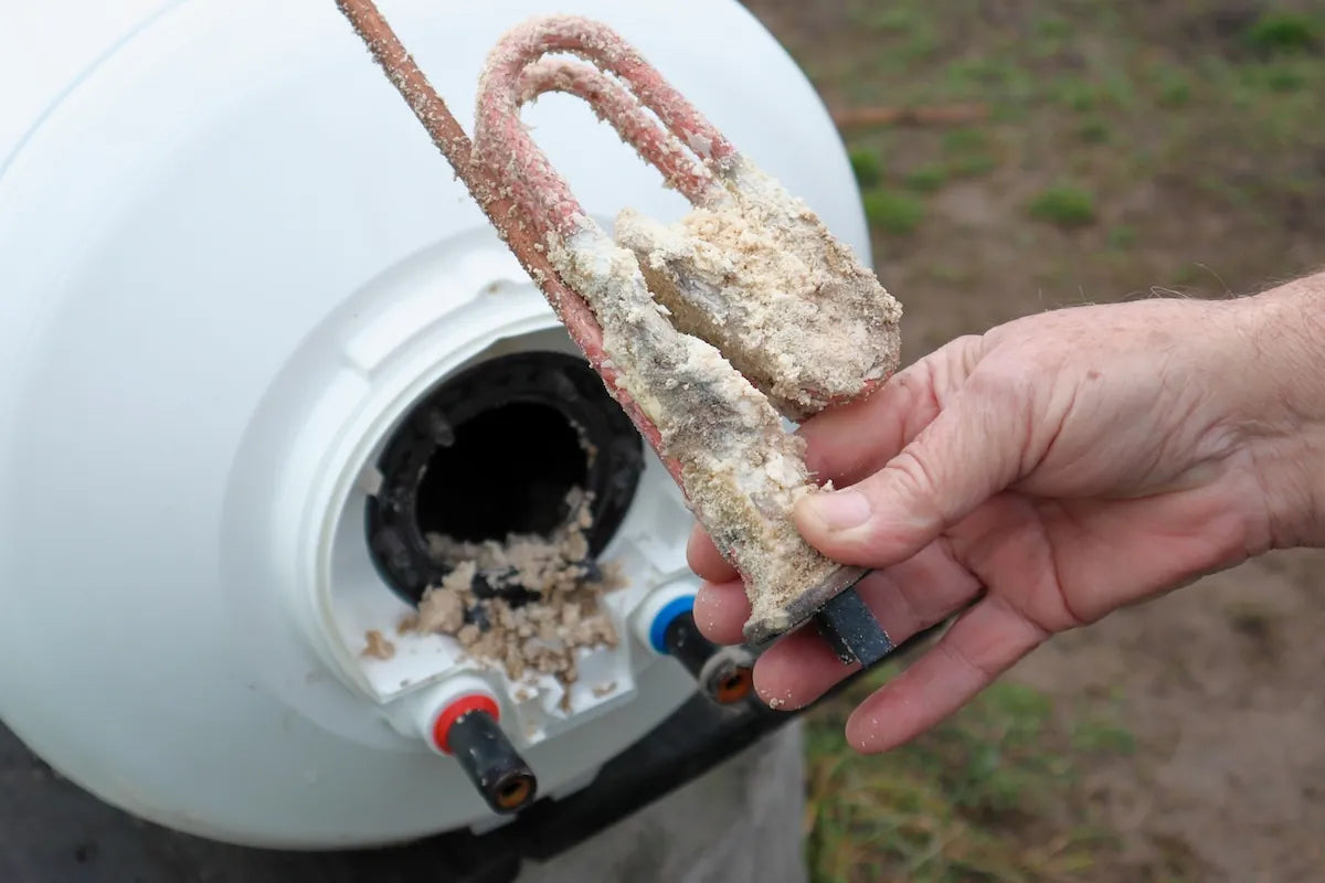 Water heater heating element pulled from the tank, thickly caked in beige mineral scale