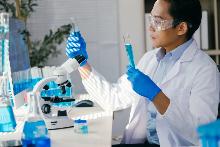Lab technician in safety glasses and blue gloves examining water samples in test tubes beside a microscope