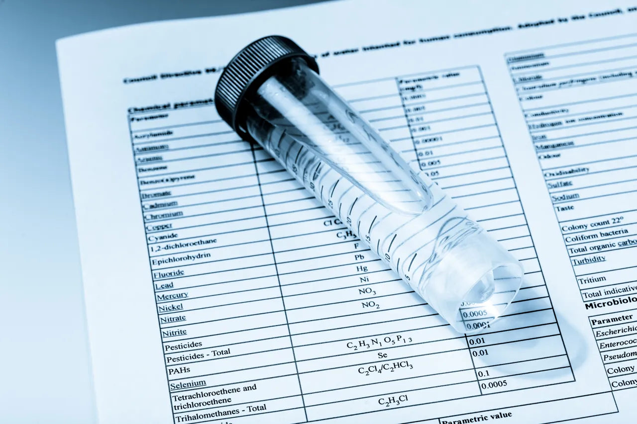 Water sample test tube resting on a blue-toned water-quality report listing contaminants, the kind of lab analysis a TDS meter cannot replace
