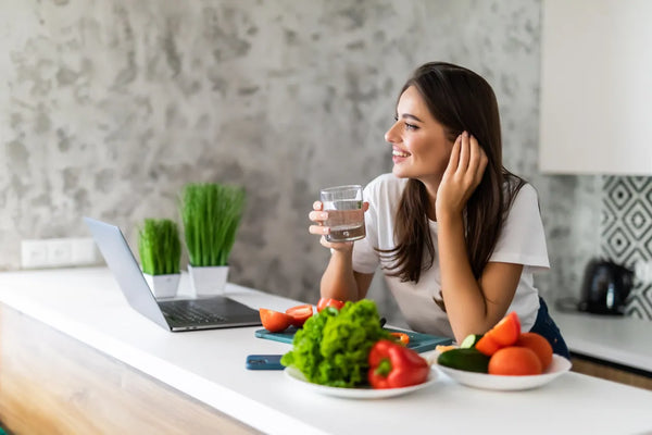 Health-conscious woman drinking a glass of water in her kitchen beside fresh vegetables