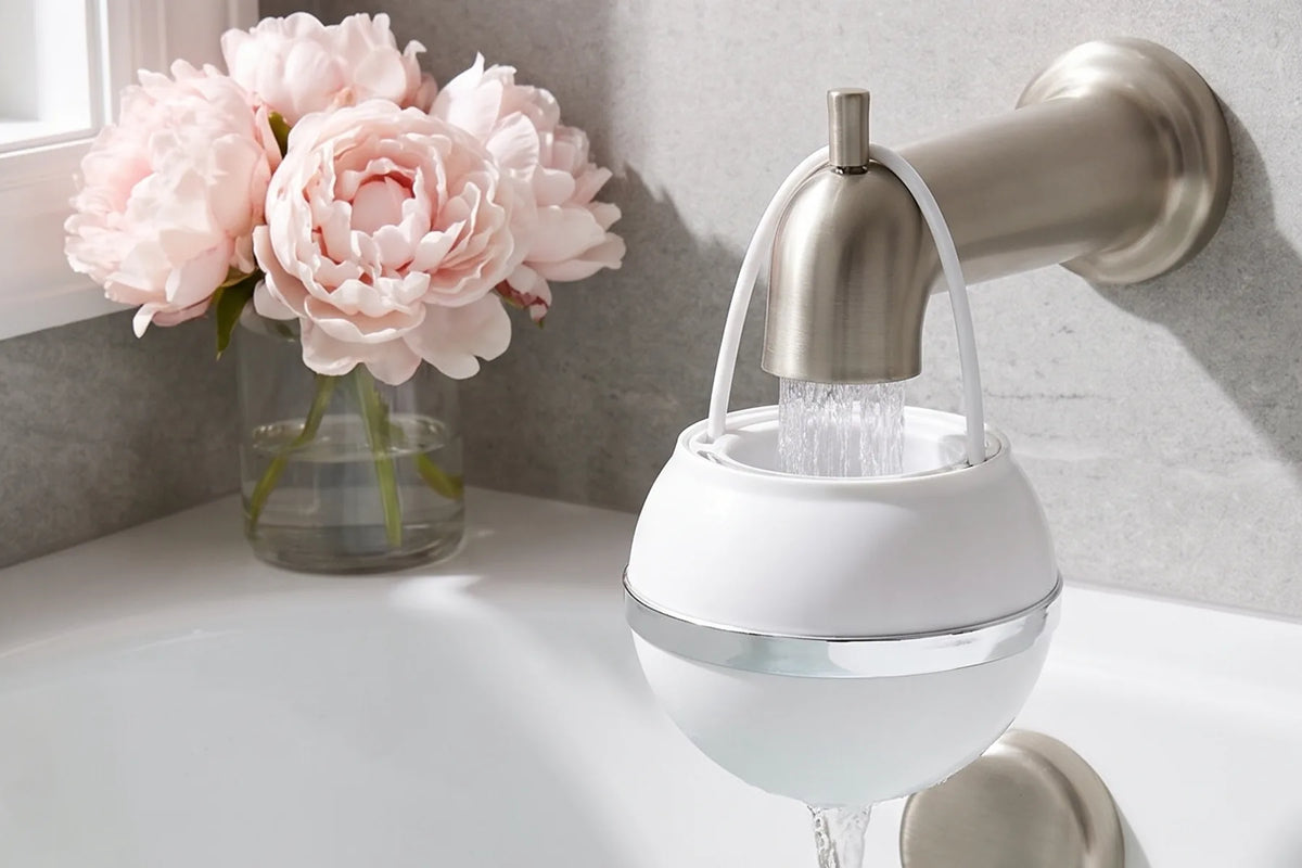 White Bath Ball hung on a brushed nickel tub spout, pink peonies beside the bath