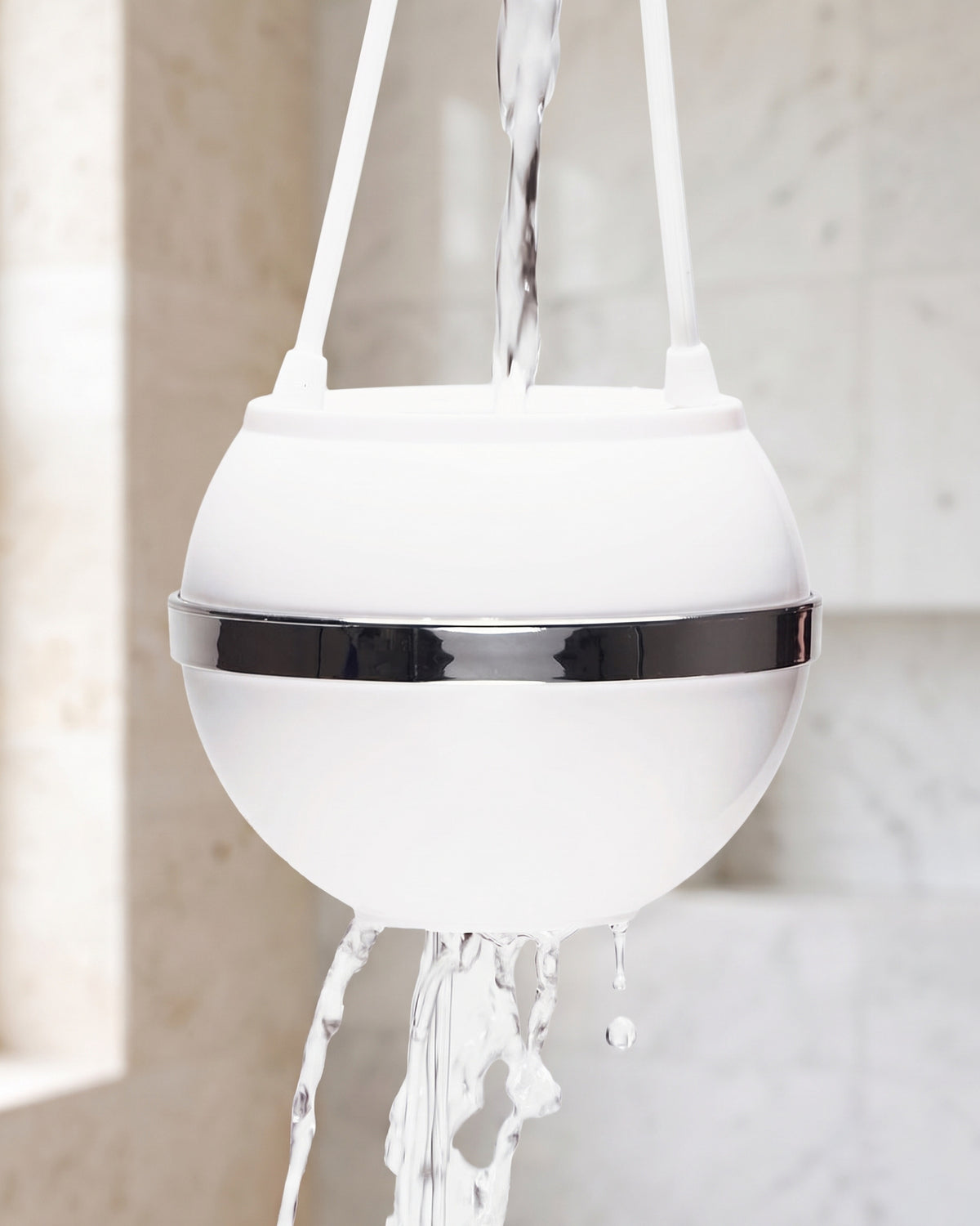 The White Bath Ball hanging by its loop, water running into its open top and out of the bottom