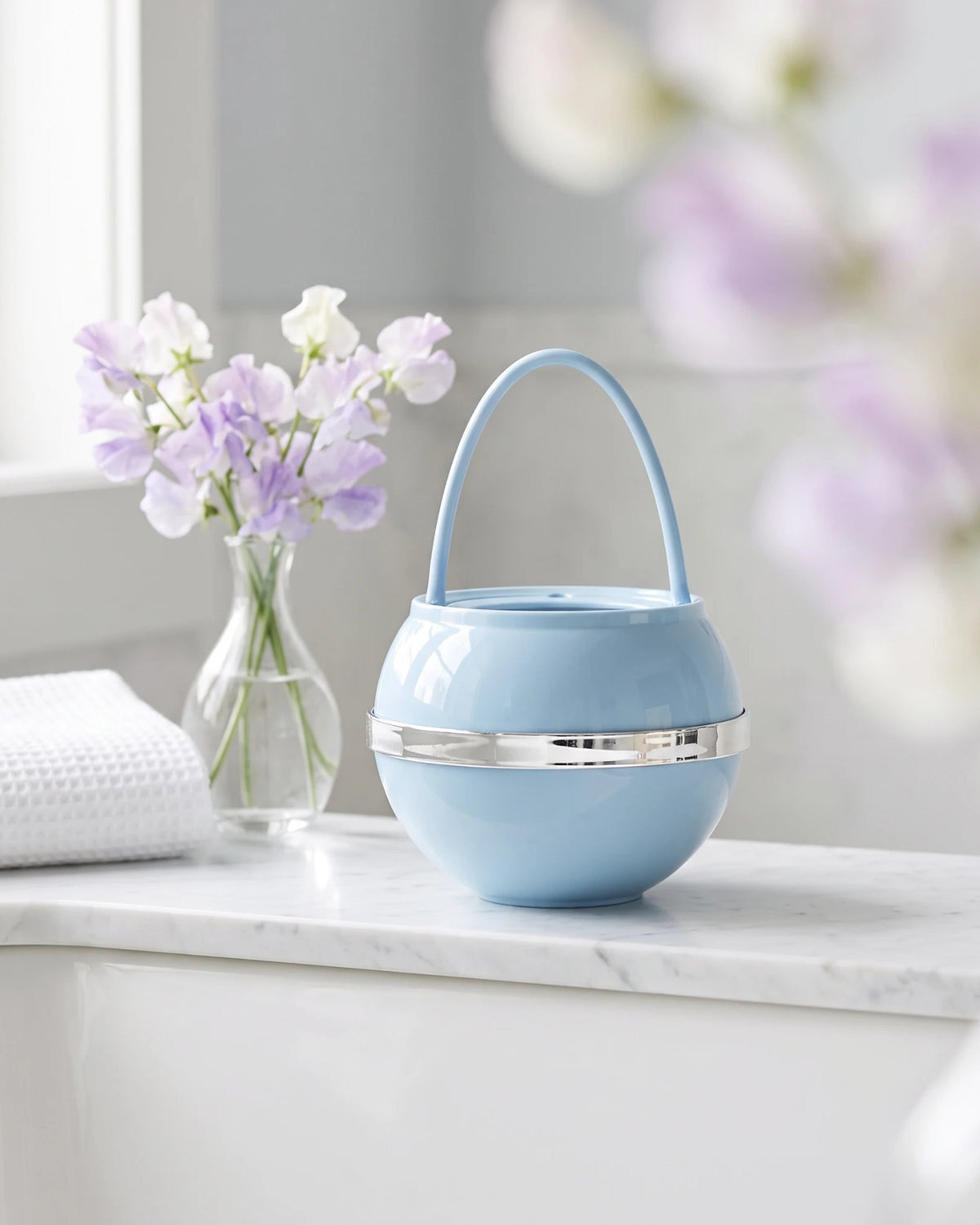 Blue Bath Ball with its handle up, on a marble tub ledge beside sweet peas and a white towel