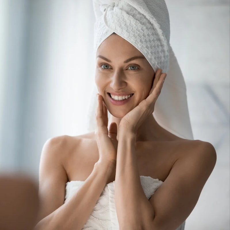 Smiling woman with a towel wrapped around her hair, touching her face