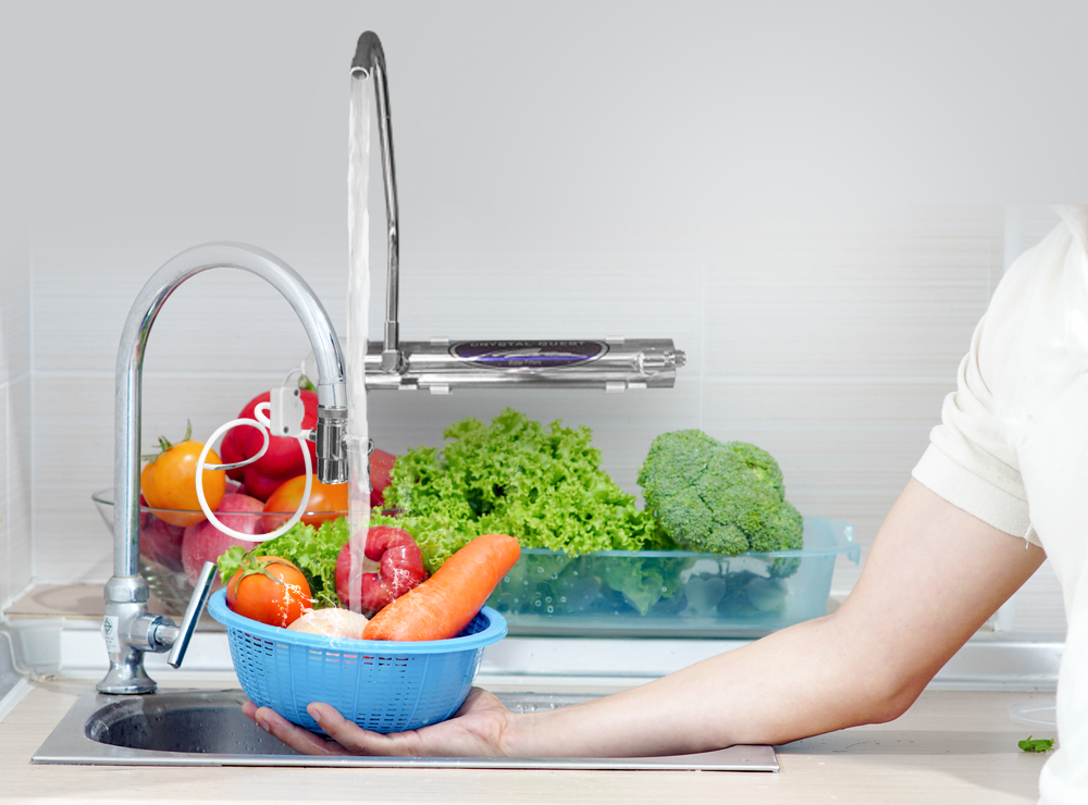 1 GPM Countertop Ultraviolet Water Sterilizer mounted by a kitchen faucet while produce is rinsed in the sink