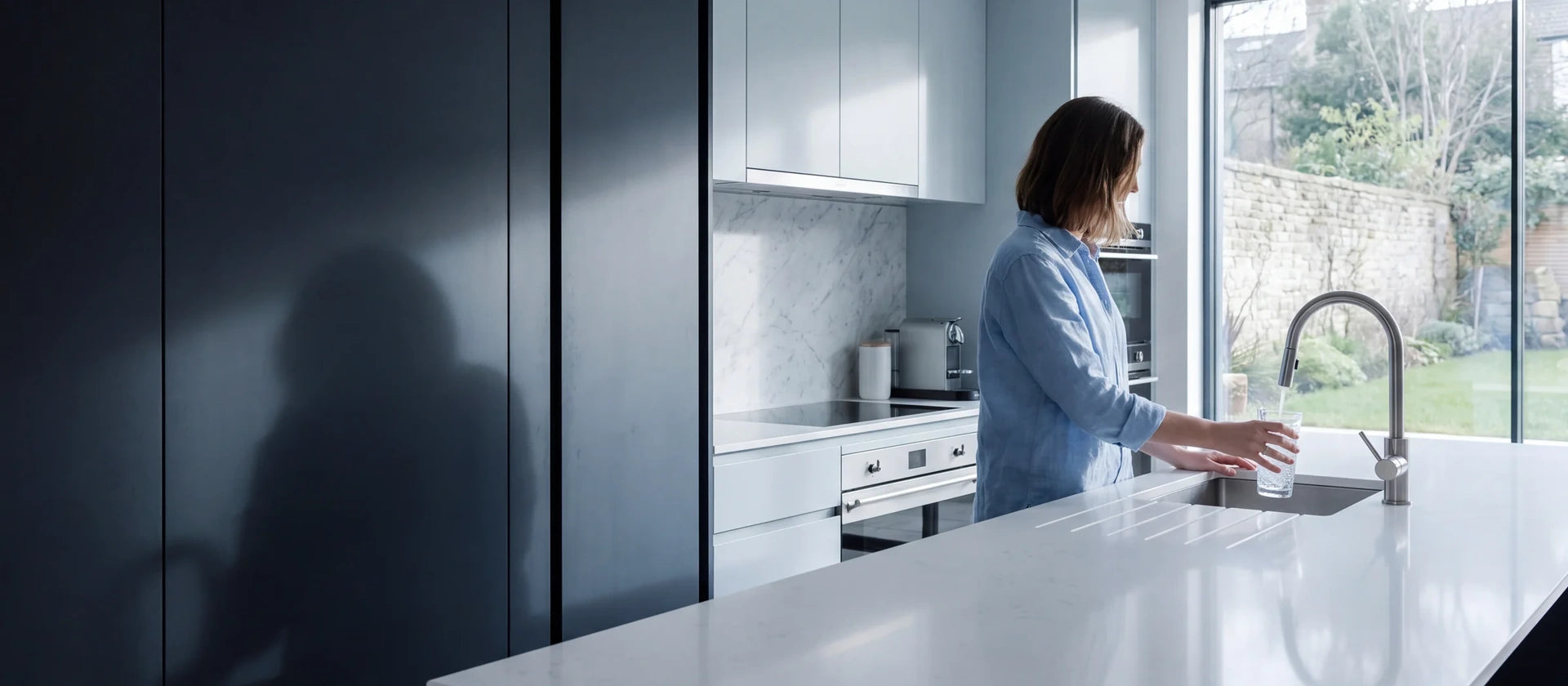 A woman fills a glass at the kitchen faucet in a bright, modern kitchen